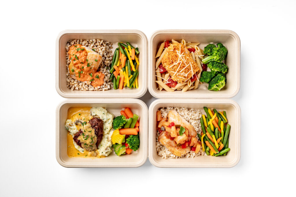 Four meal prep containers filled with dishes such as chicken with rice and vegetables, penne pasta with tomato sauce and broccoli, and mixed steamed vegetables, all set on a white background.