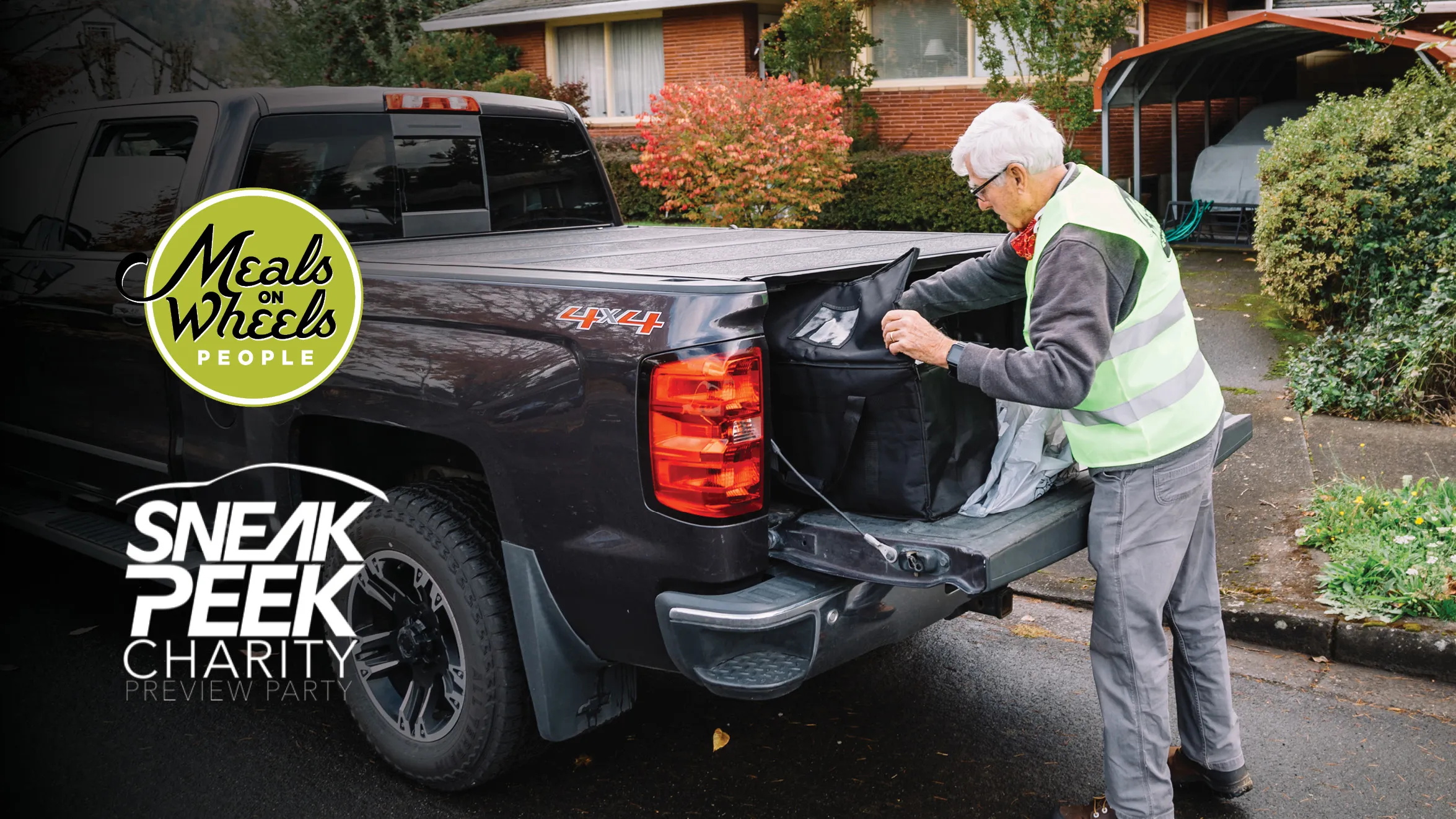 An older man wearing a reflective Meals on Wheels People vest unloads a bag from a pickup truck marked with "Meals on Wheels People" and the Oregon International Auto Show Sneak Peak Charity Event. The scene is outdoors in a residential area.