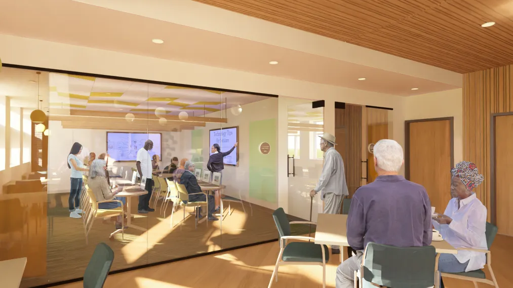 A group of older adults in the future Eastside Resource Center Tech Hub, engaged in a presentation. Some are seated while others stand. The room has a warm, inviting atmosphere.