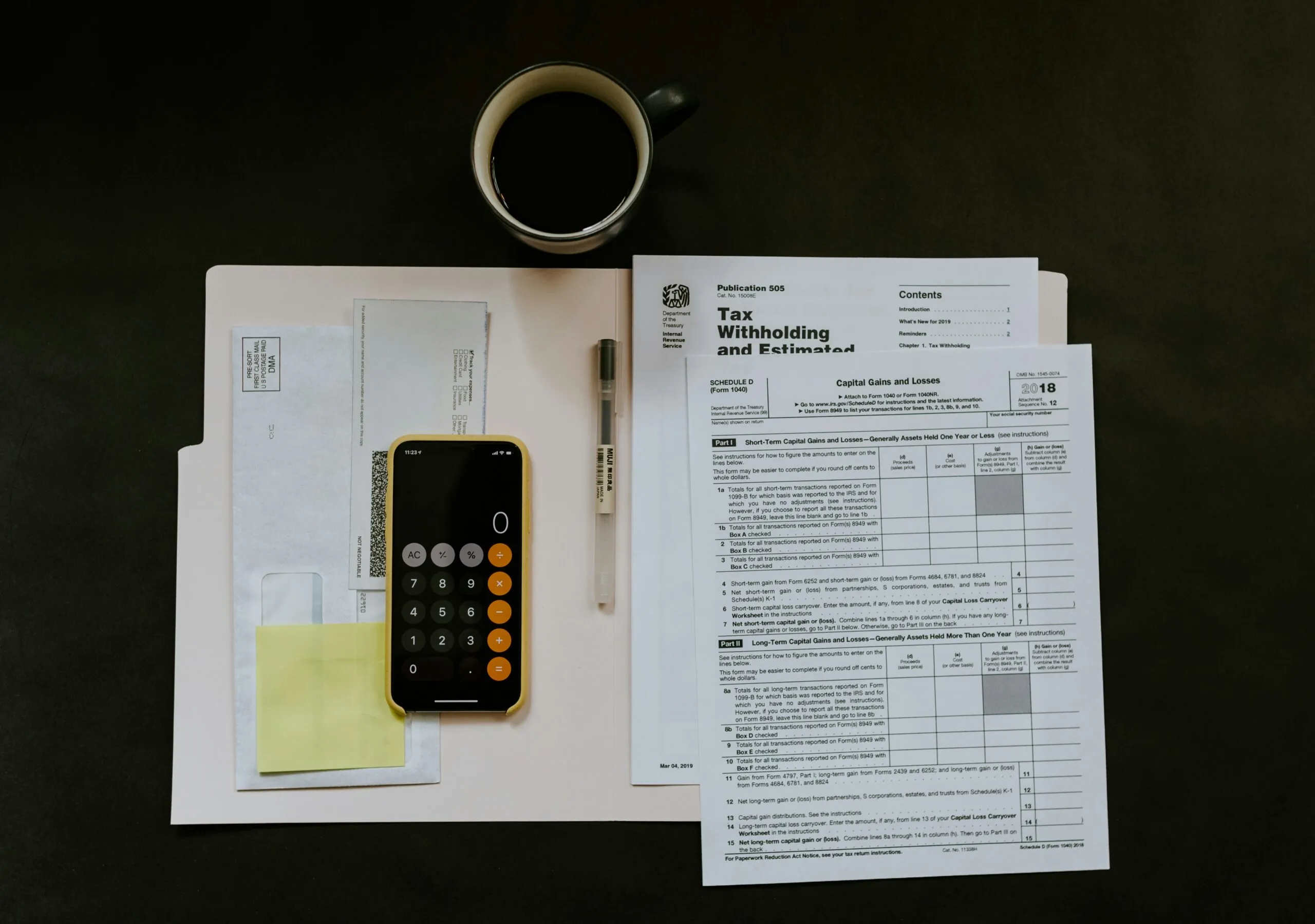 A desk with tax forms, envelopes, and a smartphone calculator. A pen and coffee cup are placed nearby, suggesting a focused, diligent atmosphere.